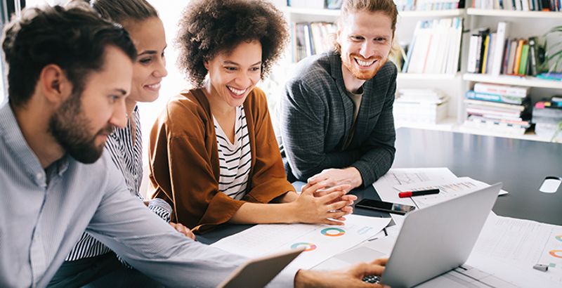 A group of people work together in front of the laptop, smiling happily